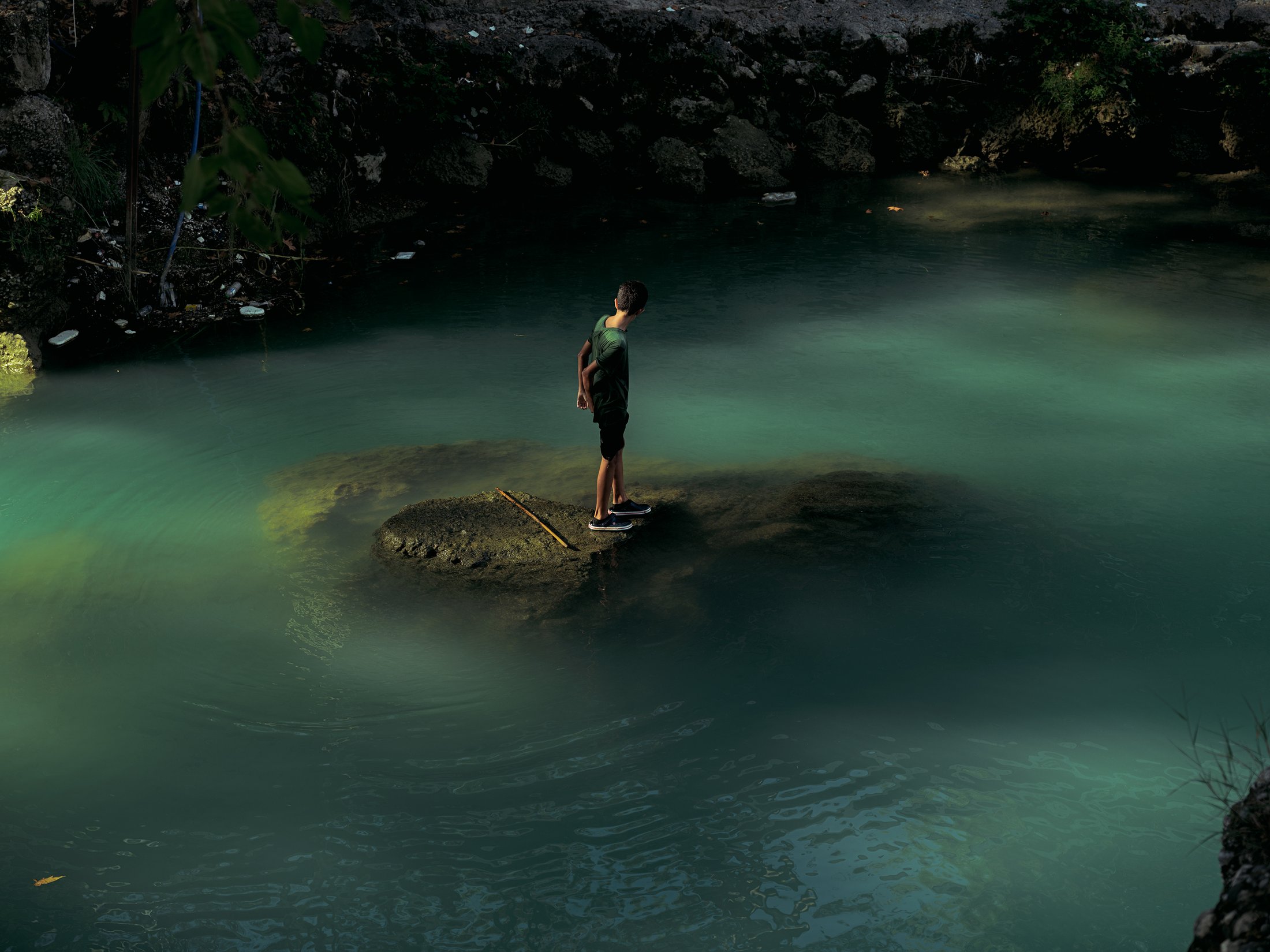 A boy standing on a rock in a green, mist-covered pool of water