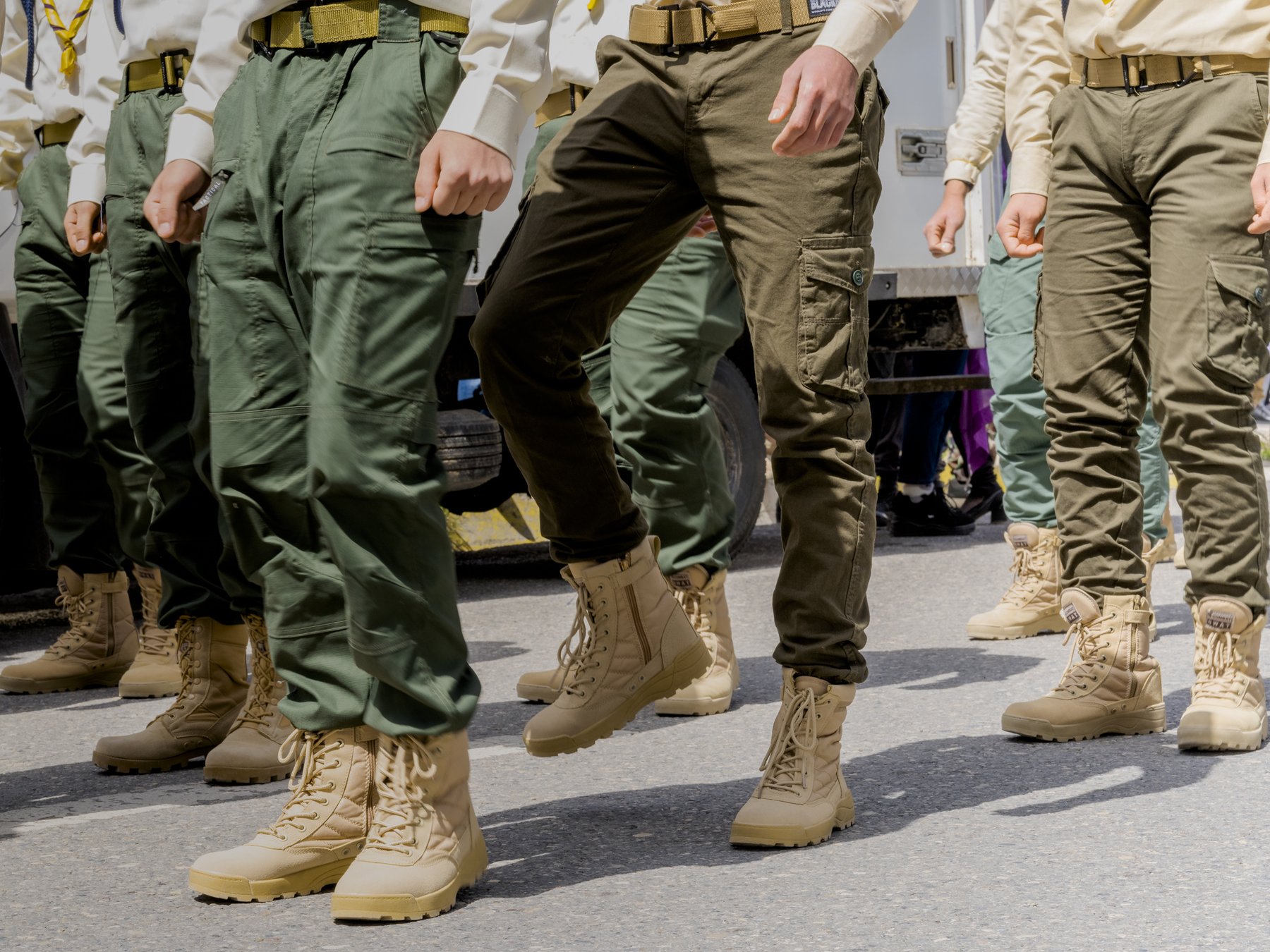 Detail of camouflage trousers and tan boots as a row of uniformed youth march in formation
