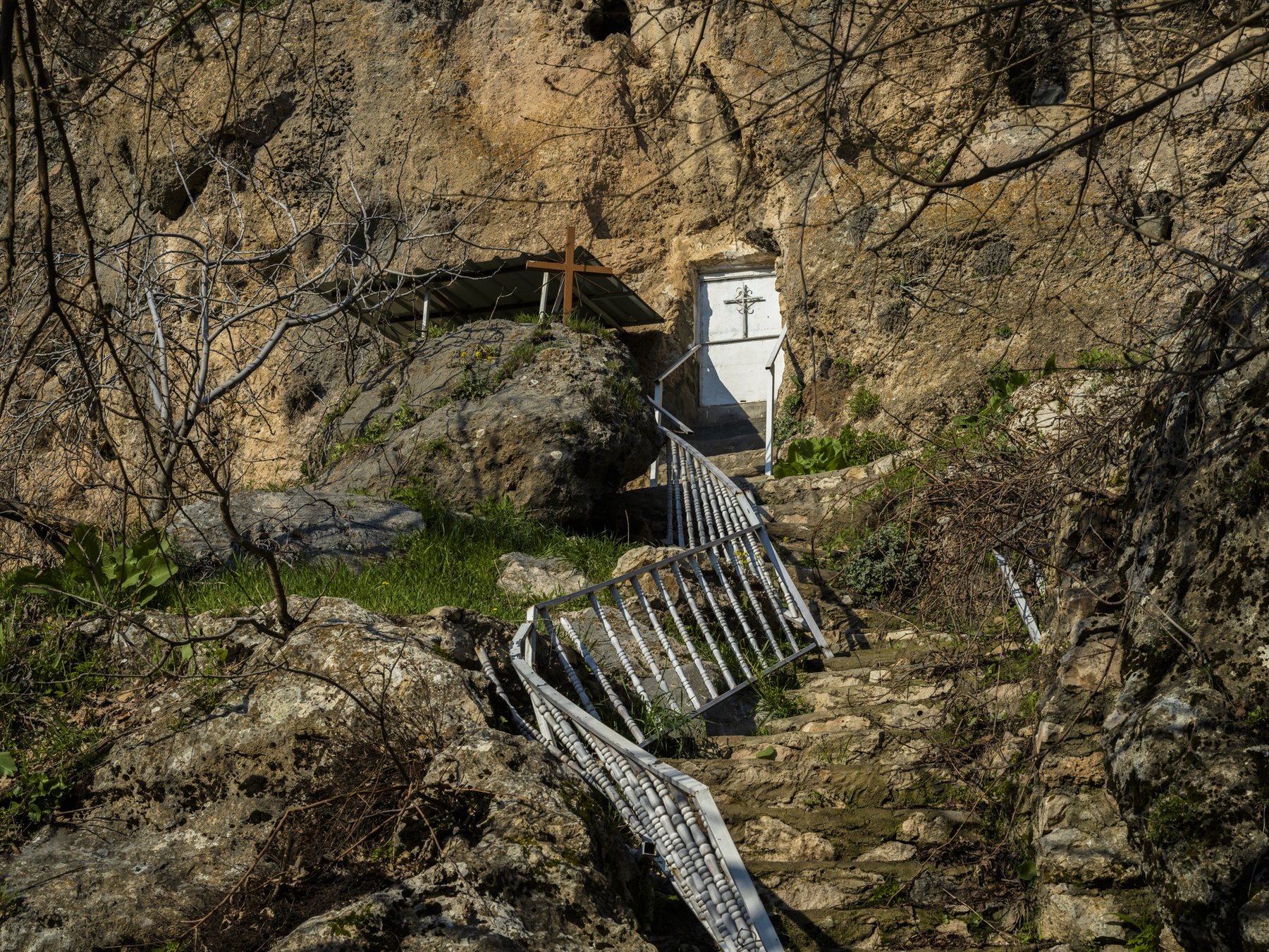 Stone steps and a railing lead up to a small white chapel door built into a rock face