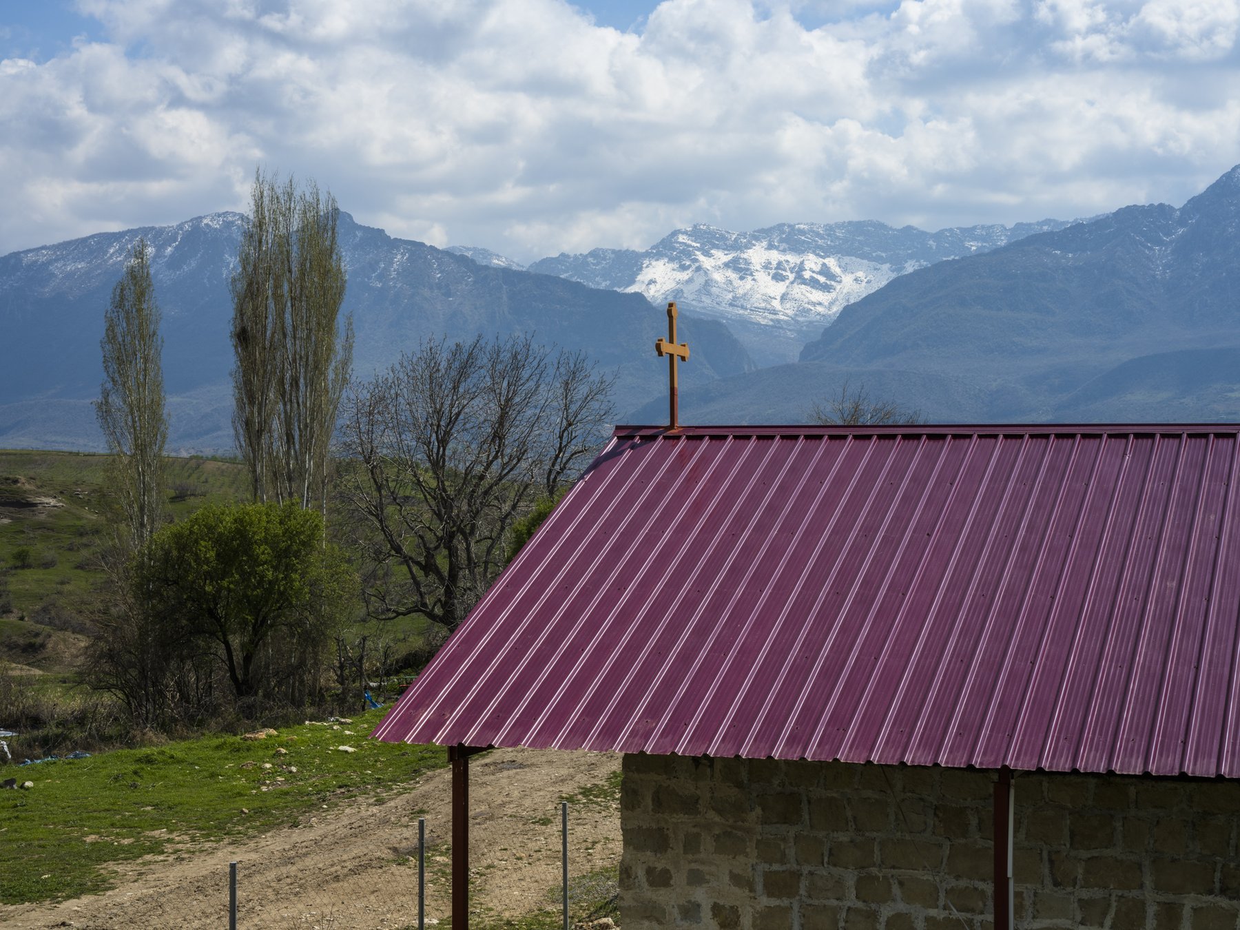 A maroon corrugated metal roof topped with a small cross, snow-capped mountains in the distance