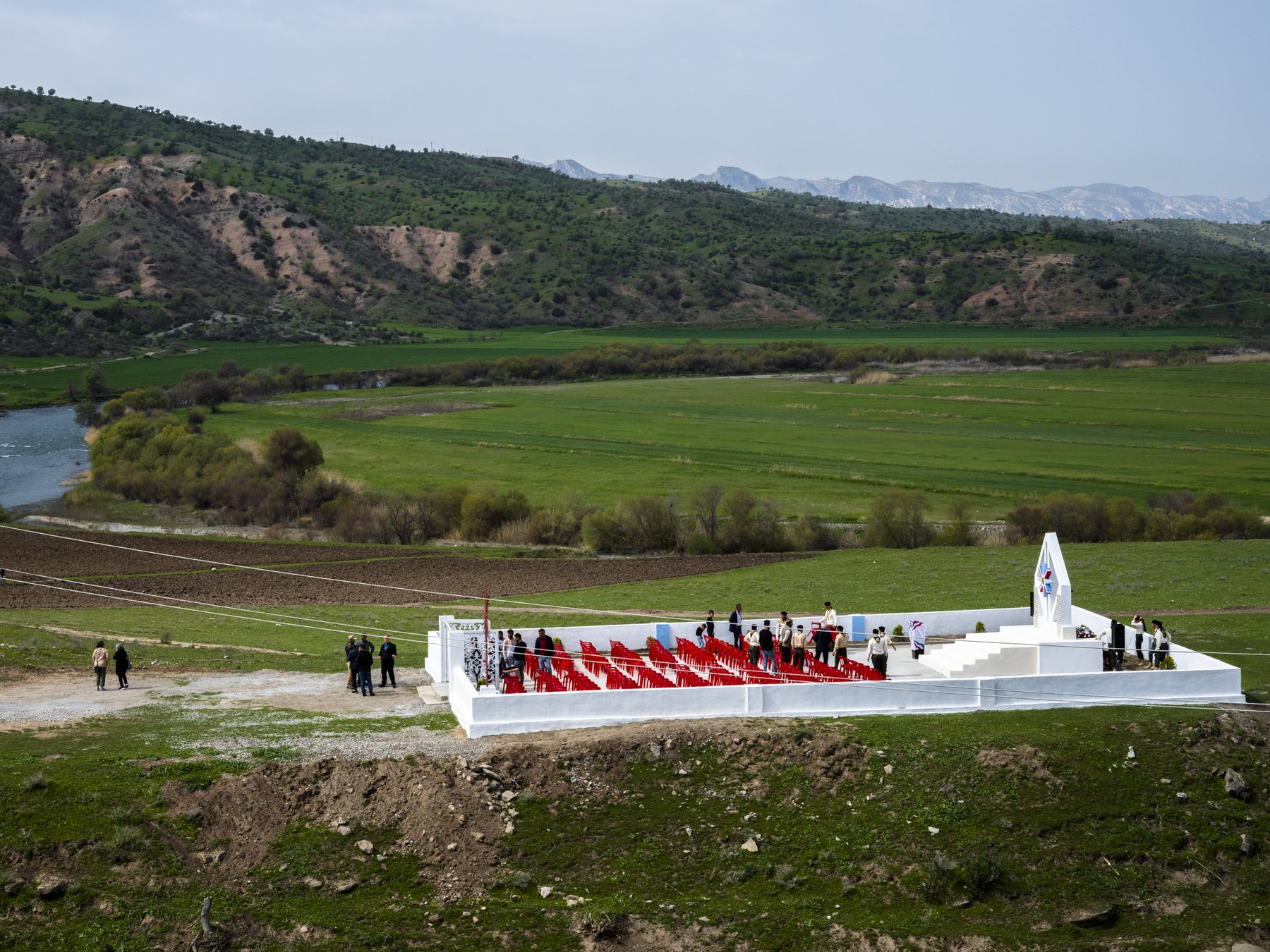 Aerial view of a white memorial platform with rows of red chairs, set in a river valley
