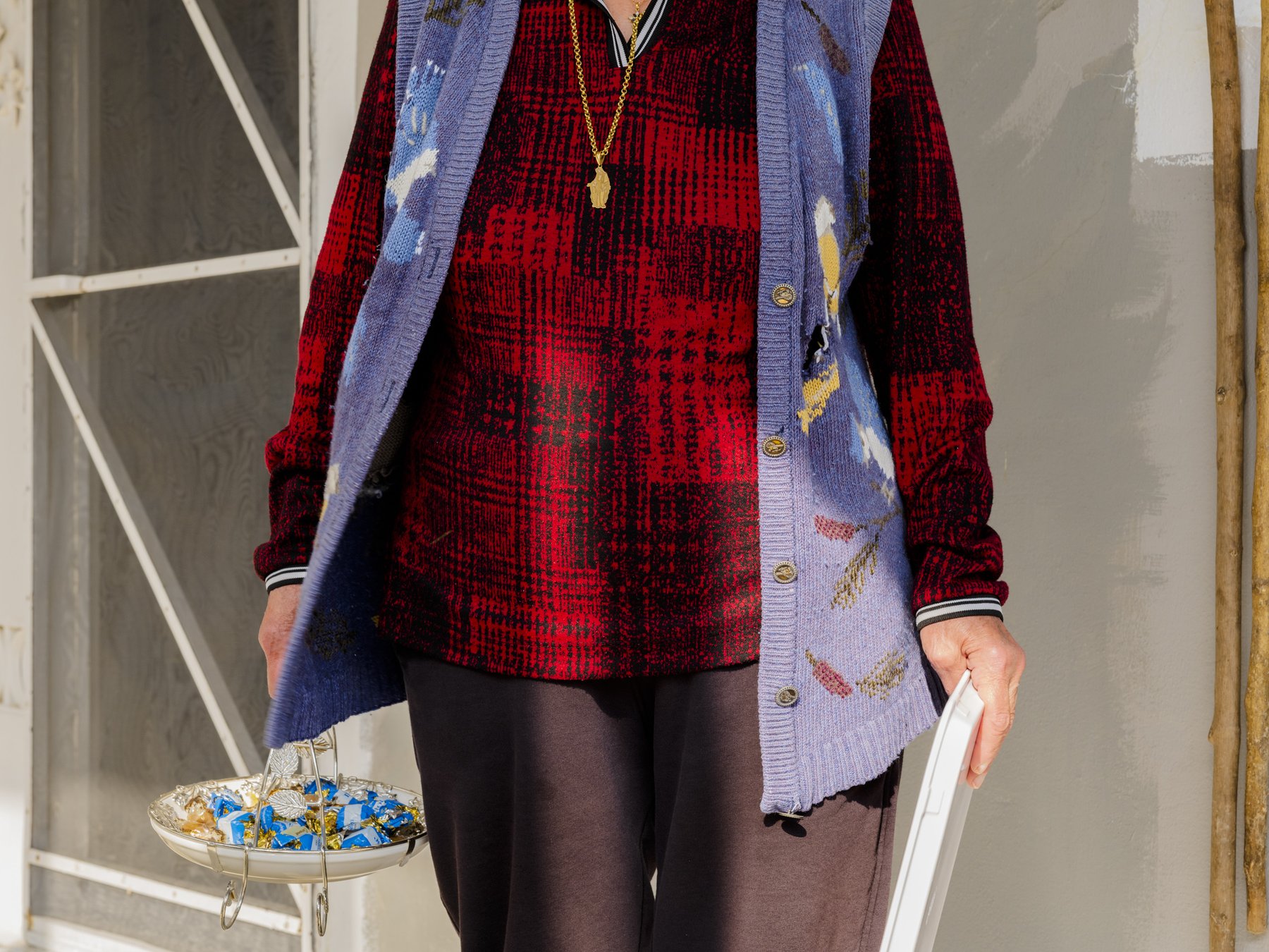 Close crop of a woman's red plaid sweater and patterned cardigan, holding a tray of sweets