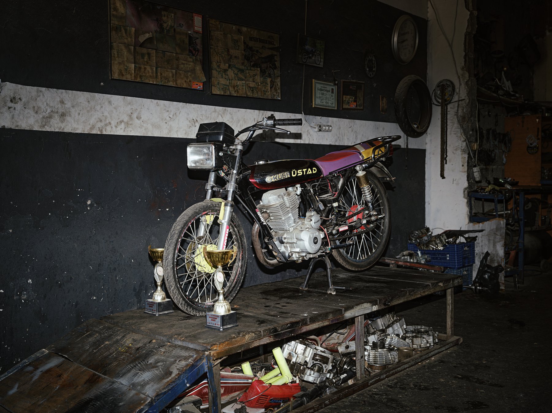 A heavily customized motorcycle on a workbench, trophies displayed beside it in a cluttered garage