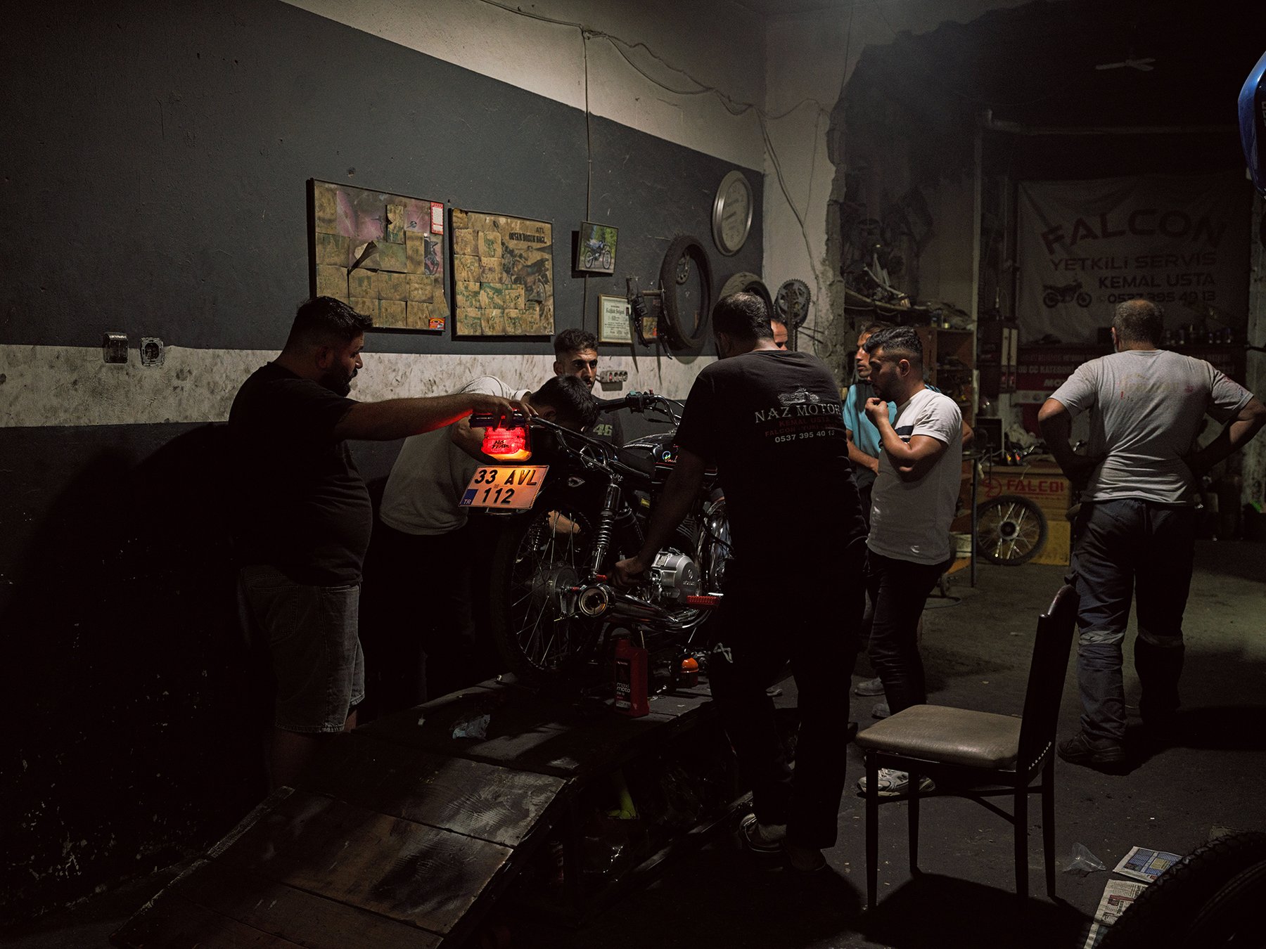 A group of men gather around a motorcycle on a workshop lift at night