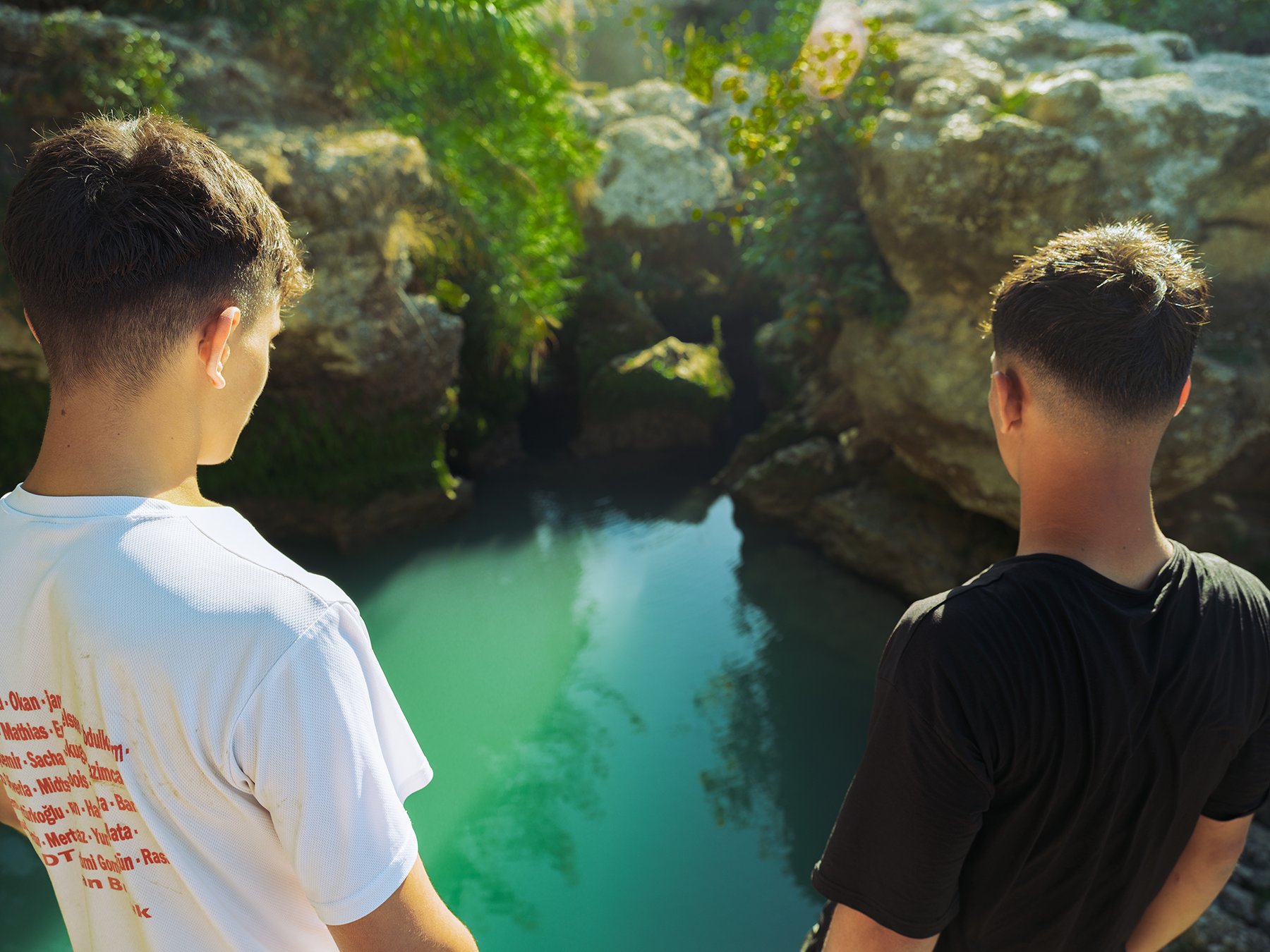 Two young men look down into a green, rock-framed pool