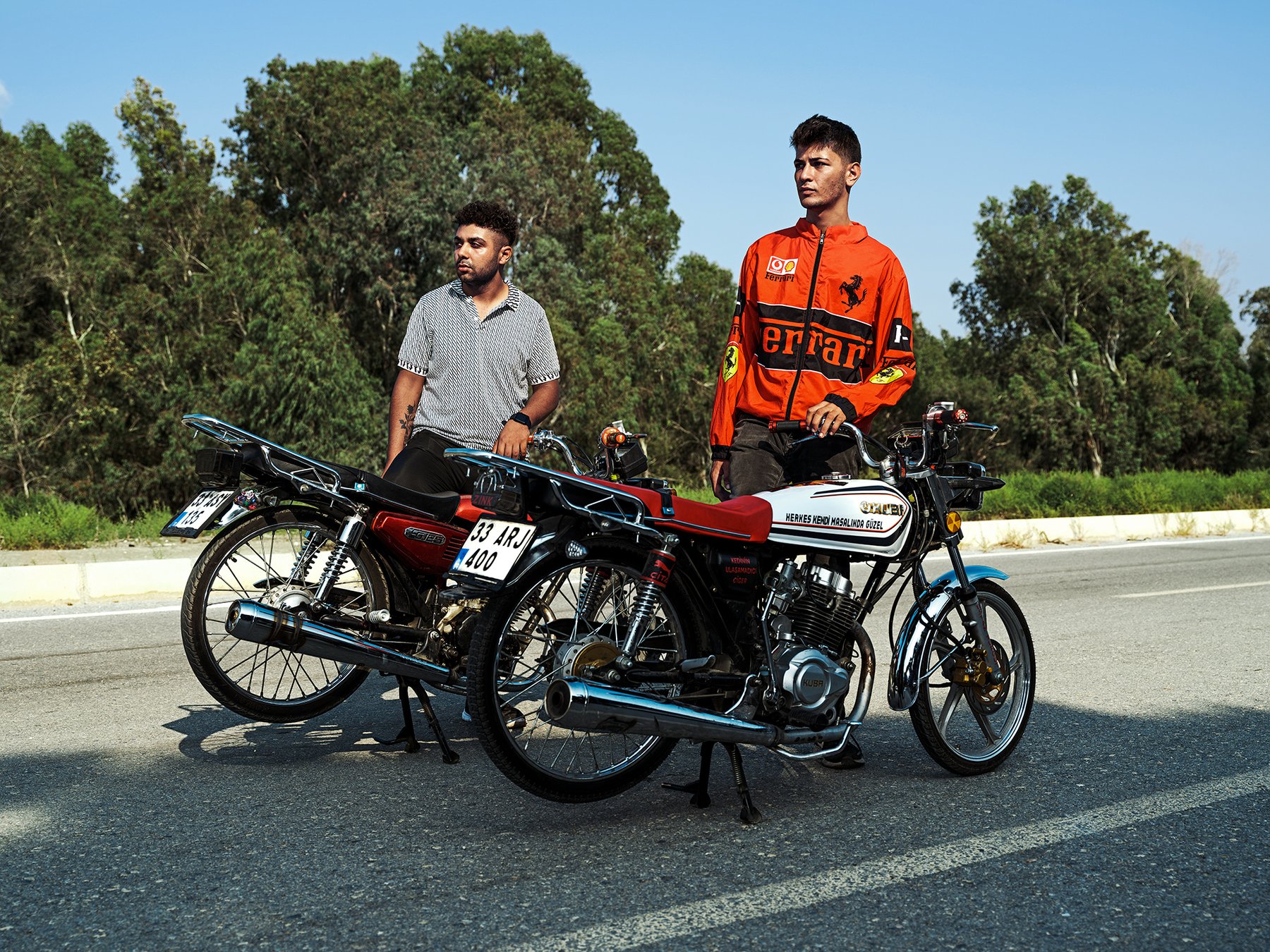 Riders perform stunts lying flat on their motorcycles as another young man walks between them