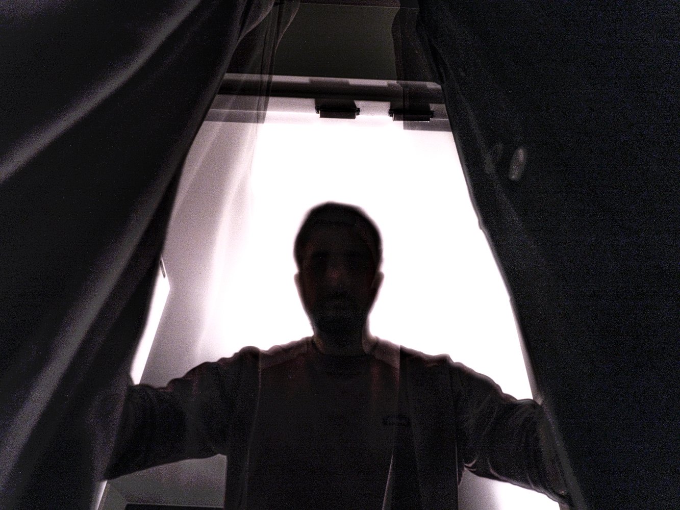 A blurred figure stands silhouetted against a bright doorway, arms spread holding open dark curtains
