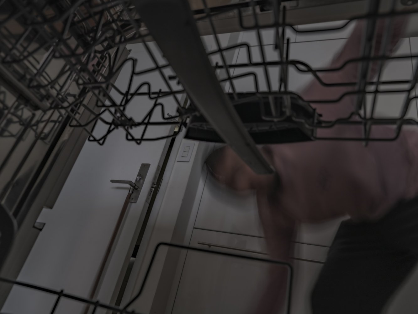 A blurred hand reaches into an open dishwasher rack, a door and light switch visible behind