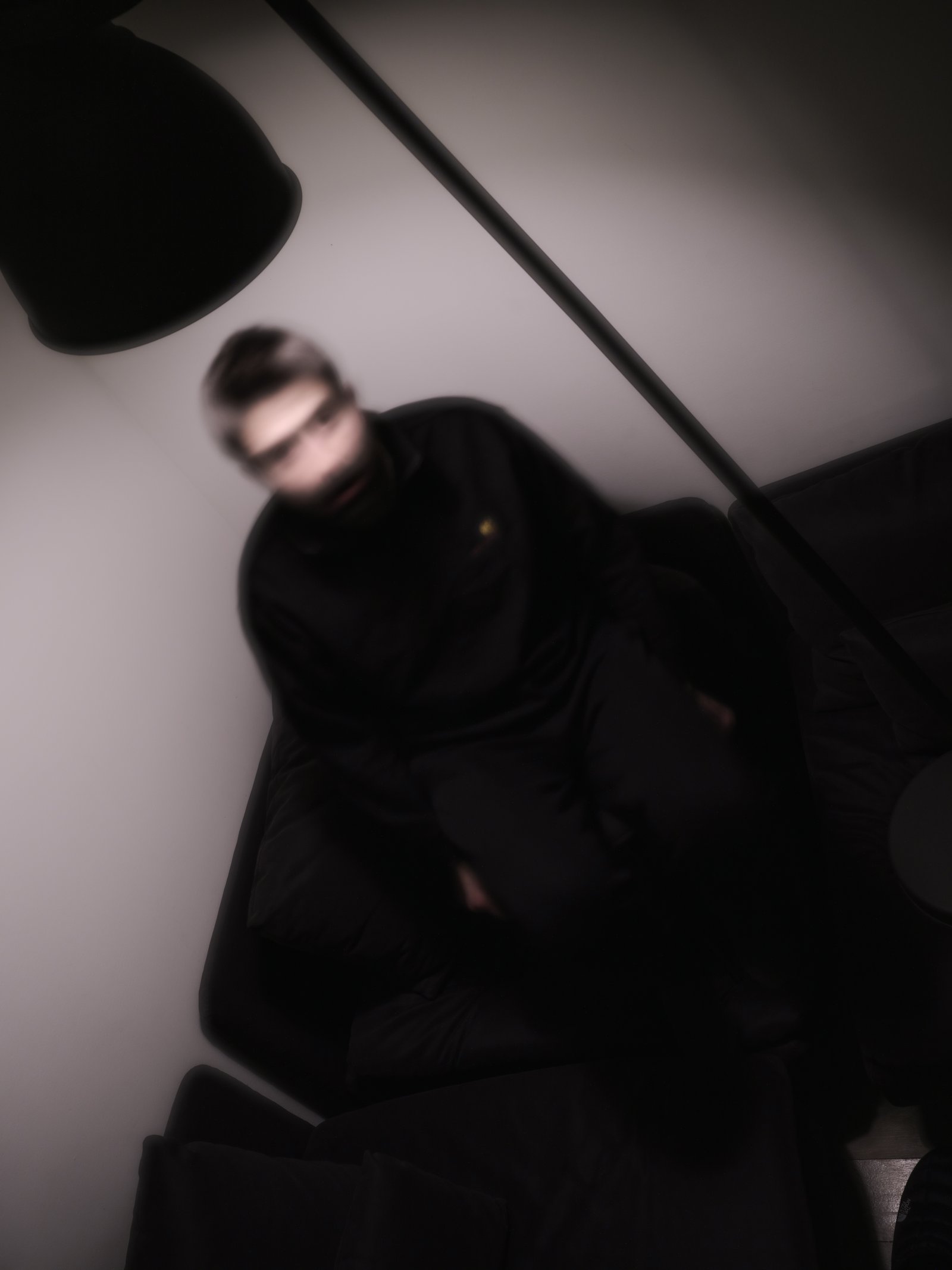 A blurred figure in dark clothing sits hunched beneath an overhead lamp