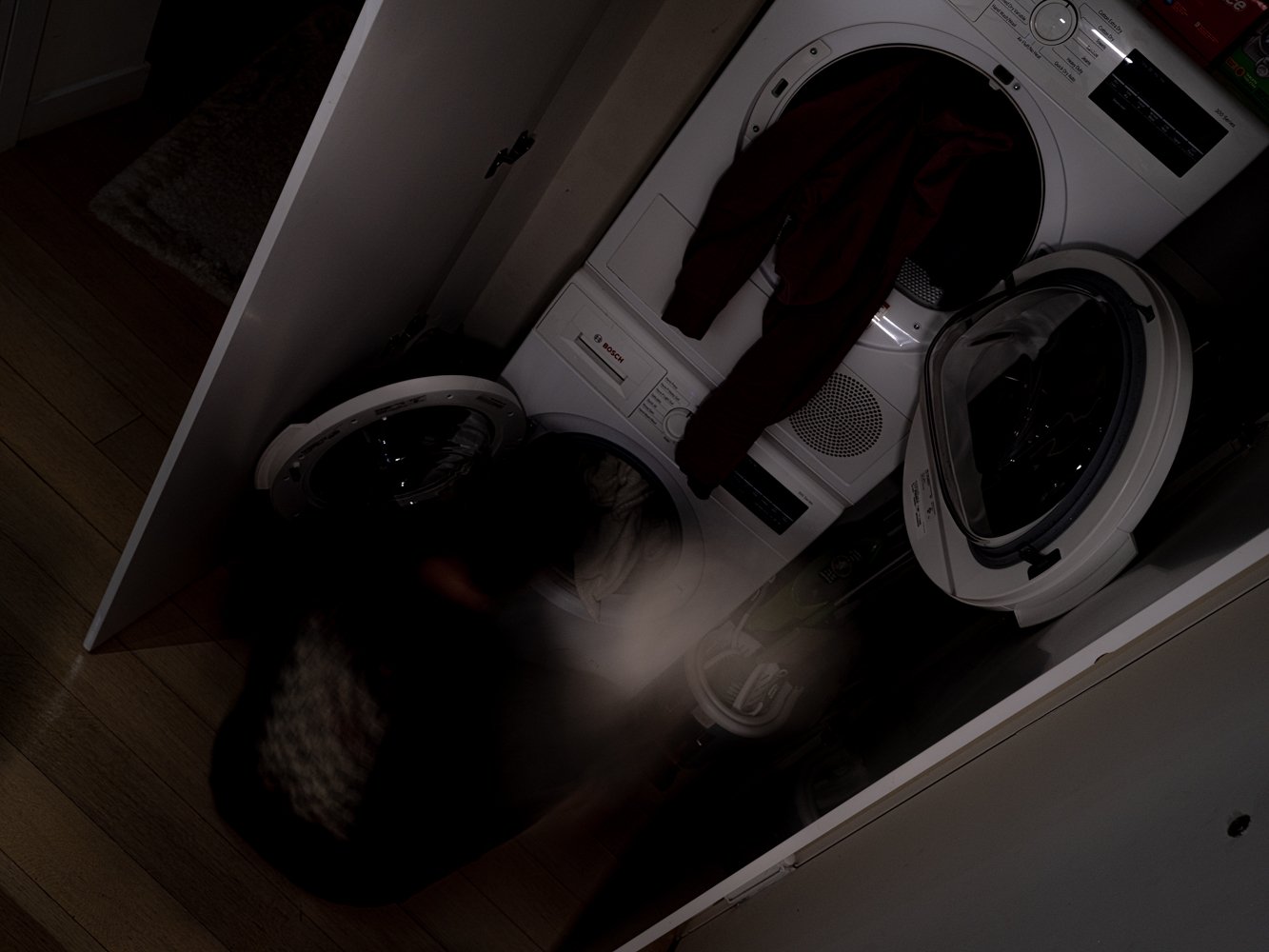 A blurred figure beside an open washer and dryer, clothes mid-tumble
